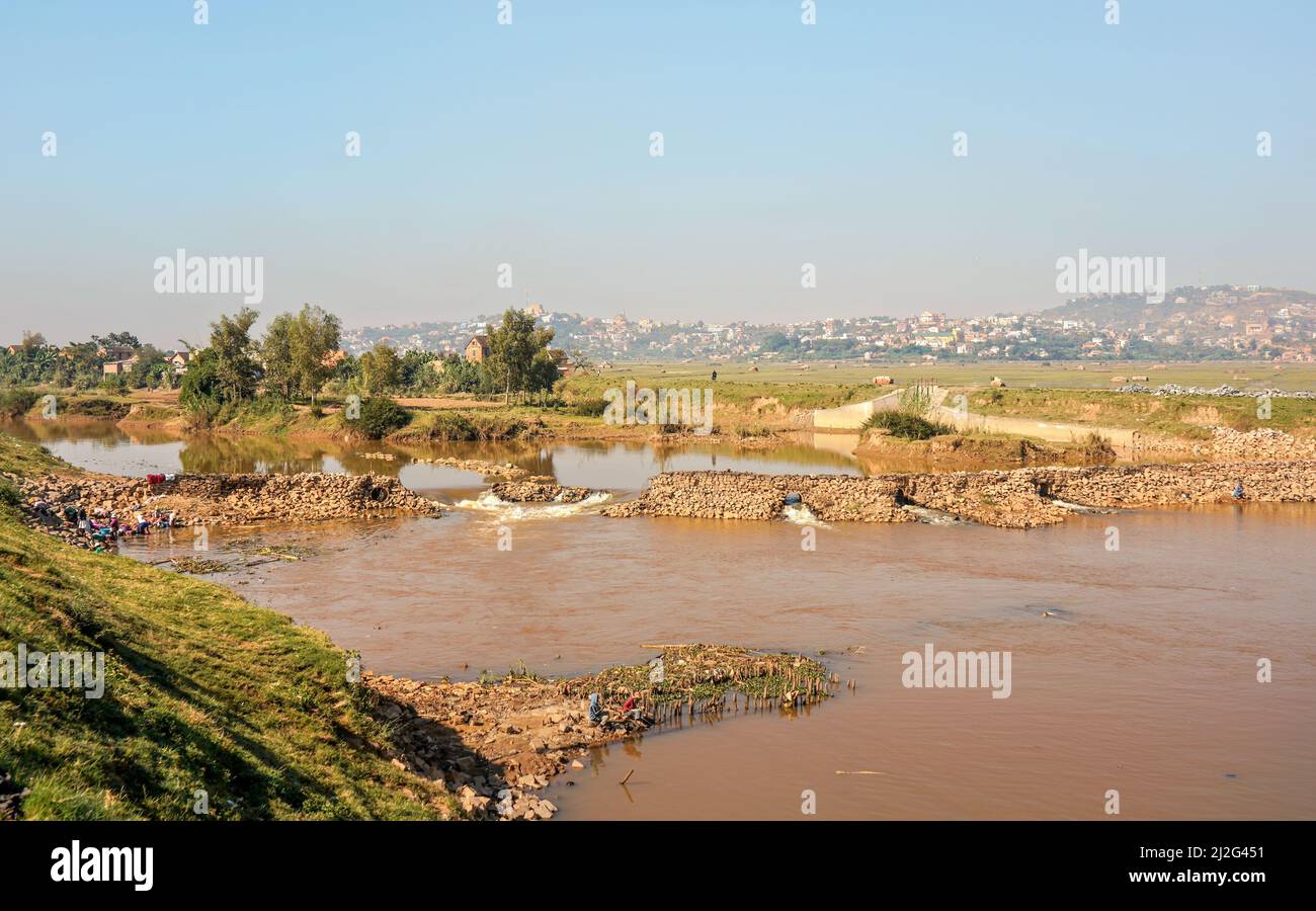 Antananarivo, Madagascar - 07 mai 2019: Personnes travaillant près de la rivière par beau temps - faire de la lessive, de la pêche, des maisons à la colline en arrière-plan Banque D'Images