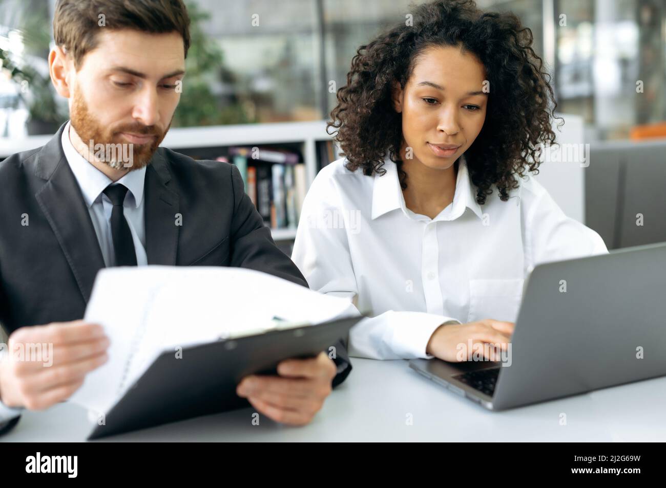 Des collègues d'affaires à succès concentrés, un homme caucasien et une femme afro-américaine, co-fondateurs d'une entreprise, travaillent sur un ordinateur portable, regardent des documents, discutent de la stratégie de développement de l'entreprise Banque D'Images