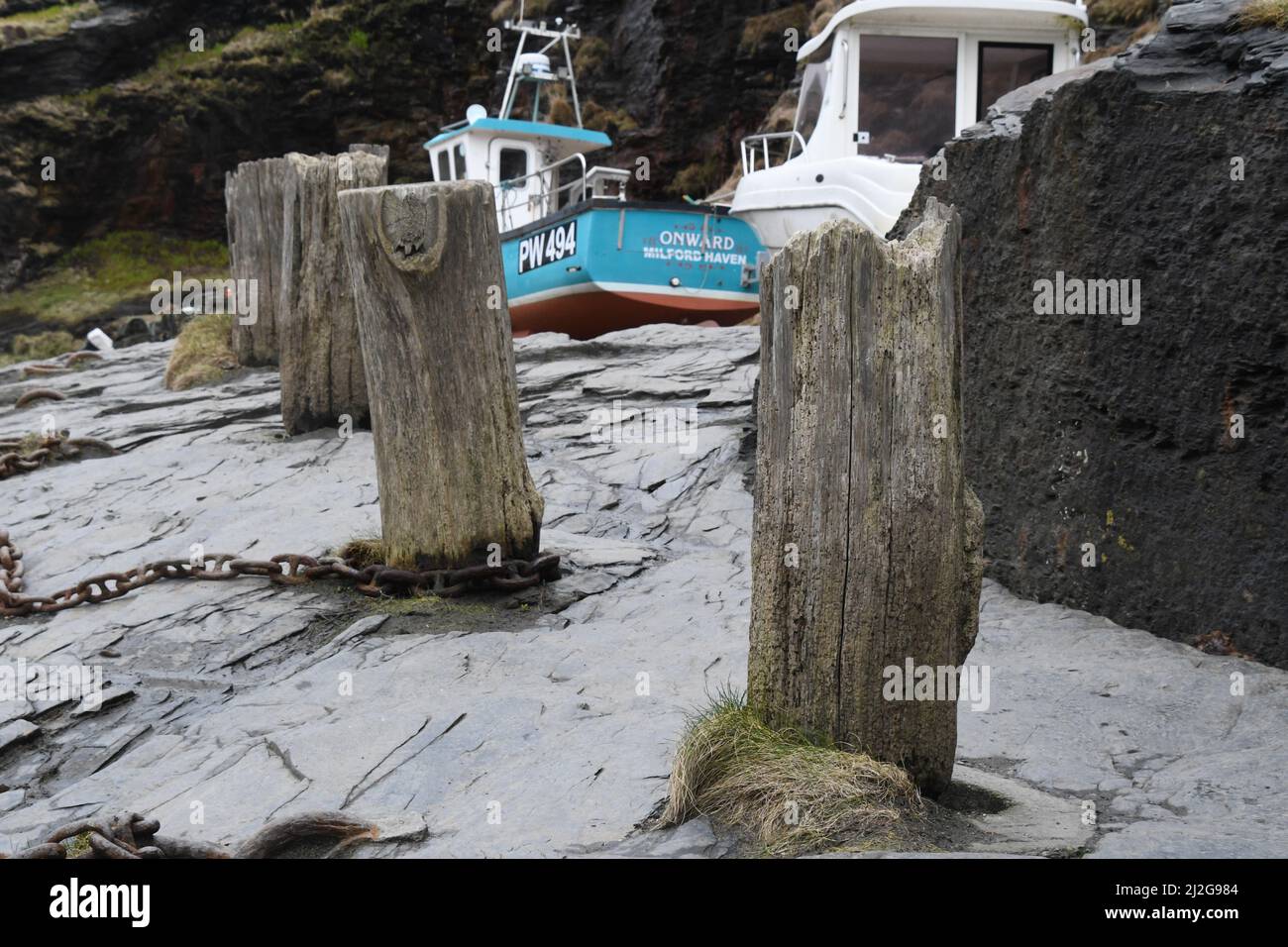 Chaîne rouillée autour de la base d'un des piquets en bois utilisés comme bornes sur le quai dans le port de Boscastle avec un bateau de pêche transporté dans le Banque D'Images