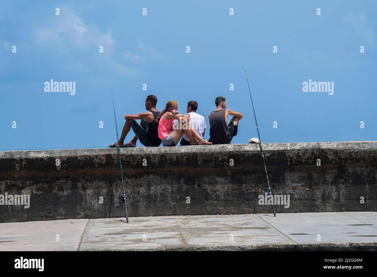 Les jeunes avec des bâtons de pêche s'assoient sur le front de mer de Malecon, attendant de pêcher dans les eaux du port en contrebas à la Havane, Cuba. Banque D'Images