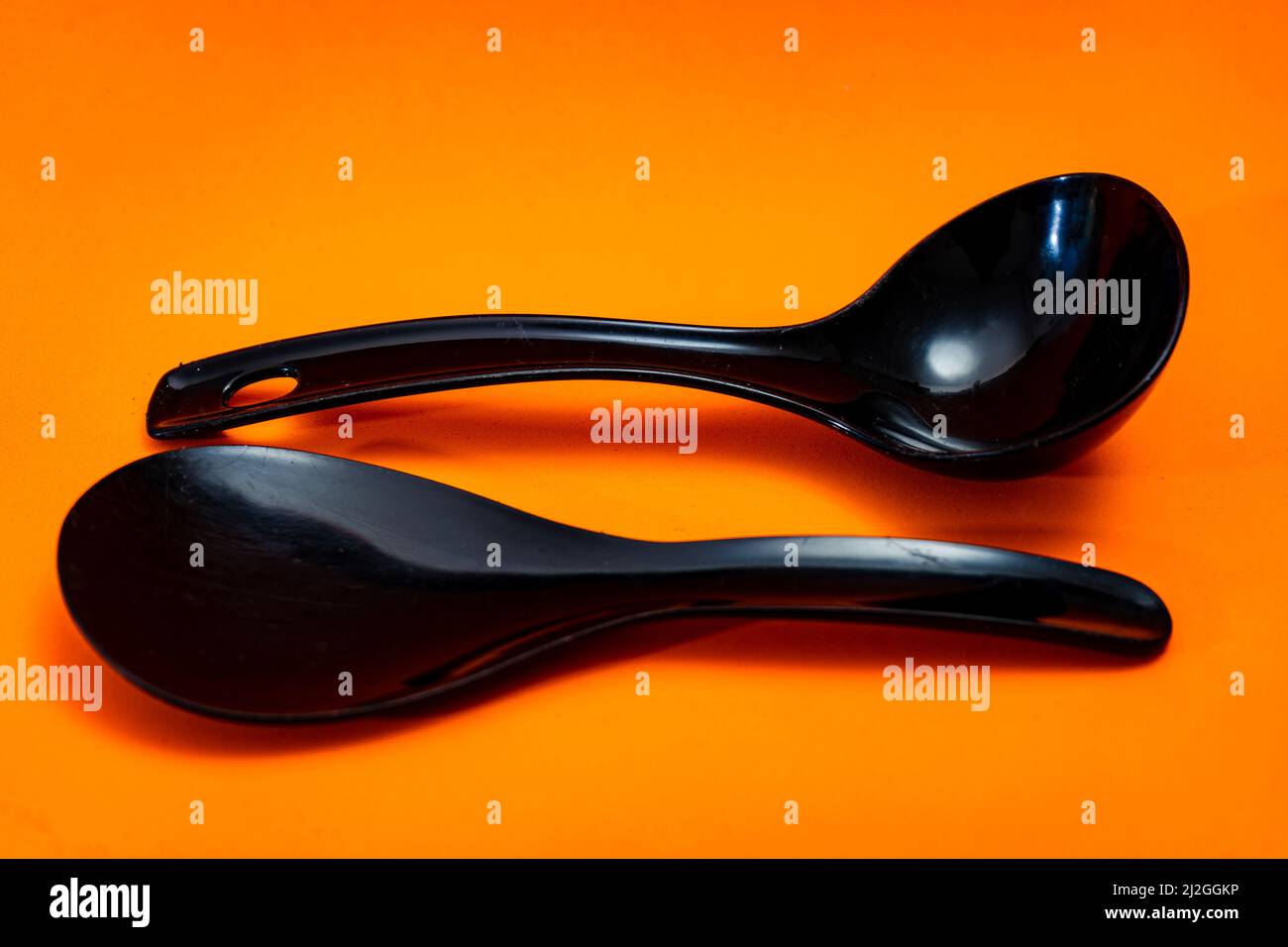 Ensemble de cuillère de cuisine et spatule en plastique noir isolé sur fond orange. Banque D'Images