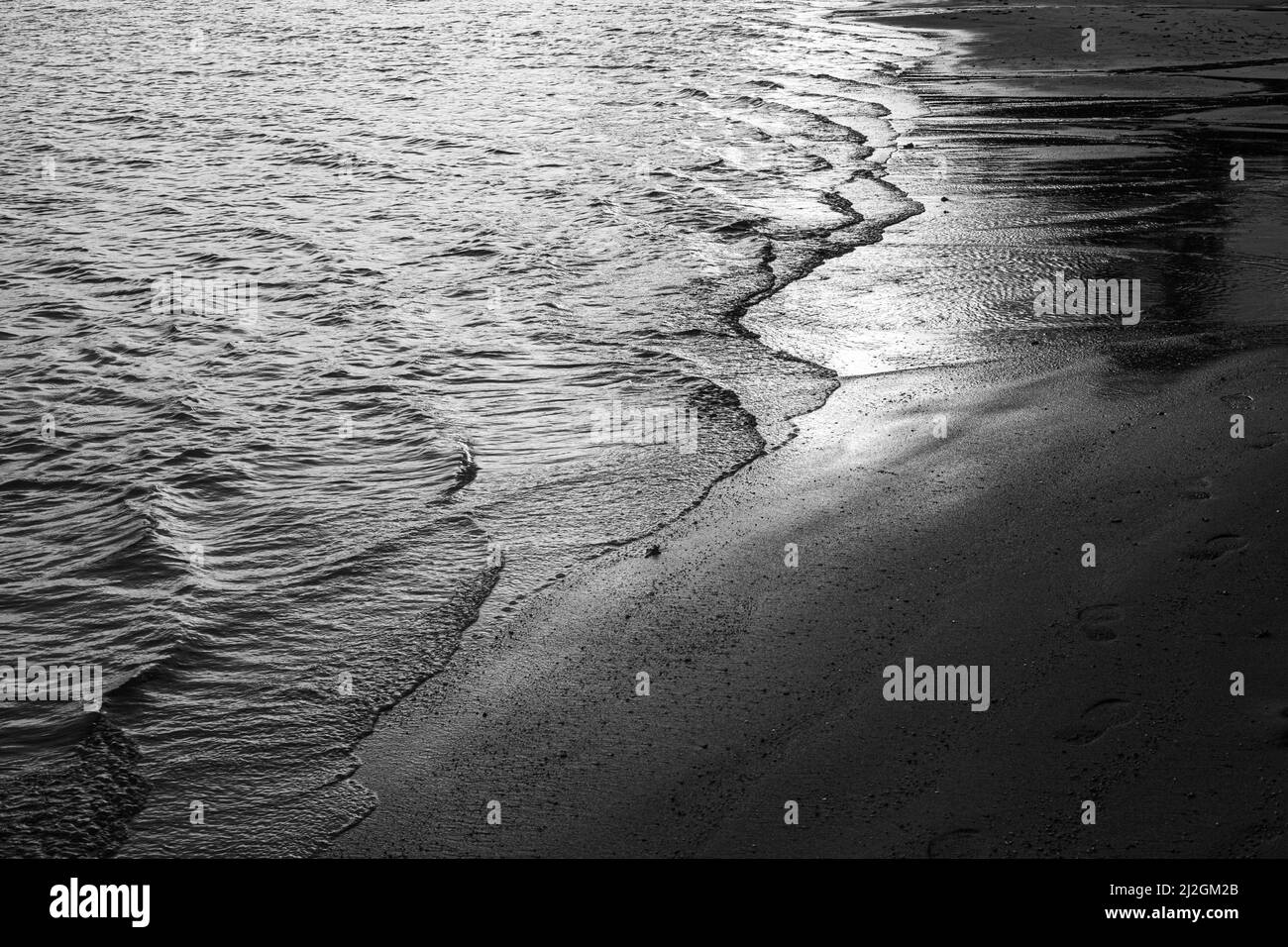 Vague d'eau de mer sur le sable. Arrière-plan noir et blanc du fluide en mouvement. Problèmes écologiques. Banque D'Images