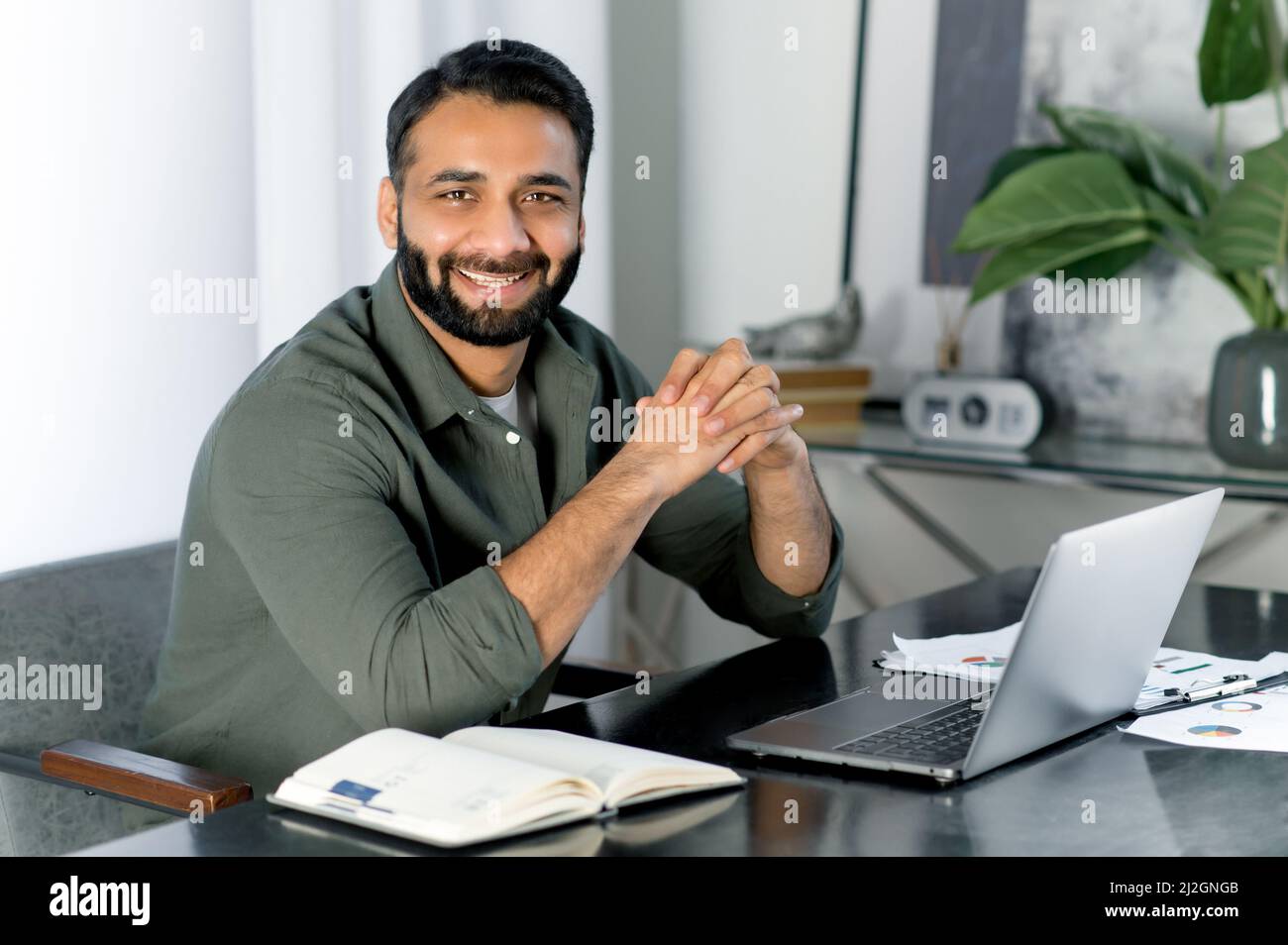Portrait d'un homme indien ou arabe créatif positif portant des vêtements élégants décontractés, directeur de compagnie, commerçant de stock, regarde directement l'appareil photo, souriant amical, assis dans un bureau moderne Banque D'Images