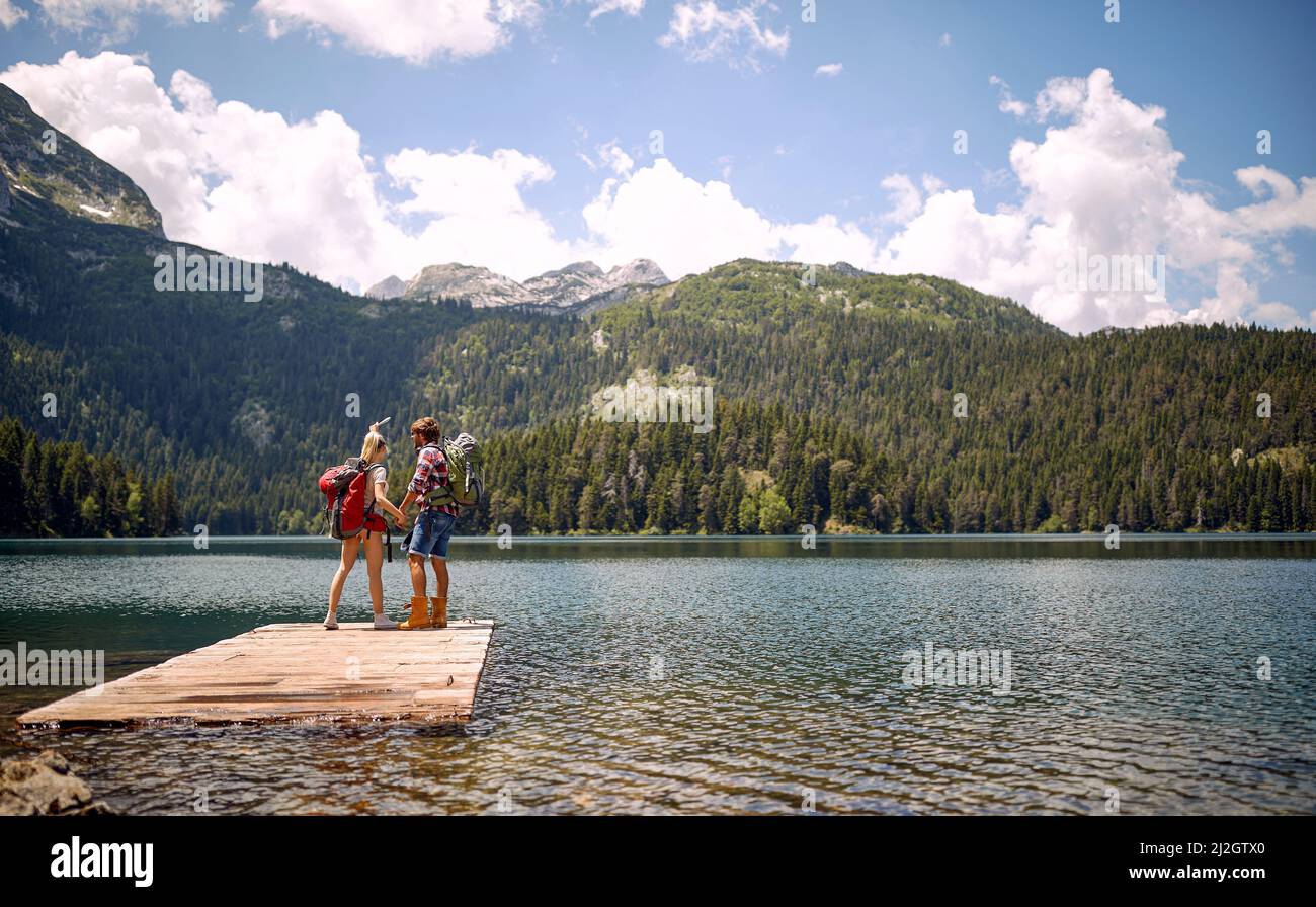 Un jeune couple se tient sur le quai au lac et profite de la vue pendant la randonnée en montagne, par une belle journée. Voyage, nature, randonnée Banque D'Images