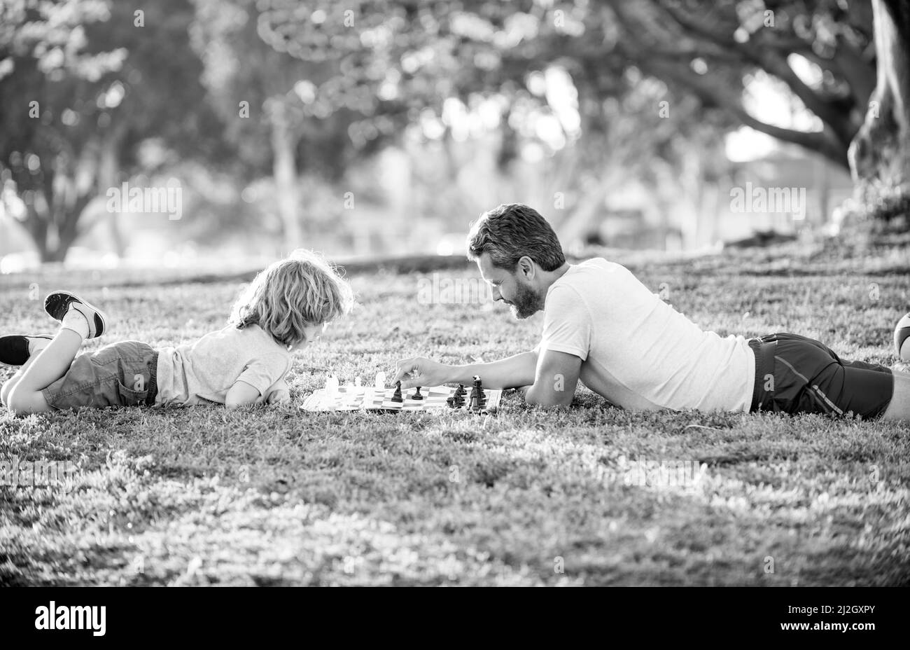 bonne famille de père et de fils garçon jouant aux échecs sur l'herbe verte dans le parc extérieur, jour des enfants Banque D'Images