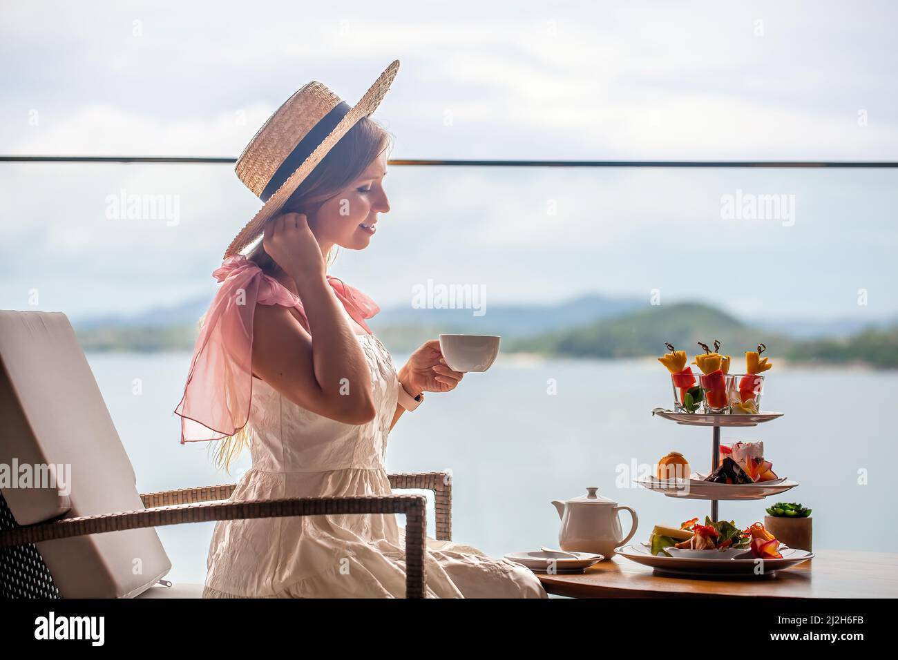 Jeune femme en robe blanche qui boit le thé de l'après-midi avec divers bonbons Banque D'Images