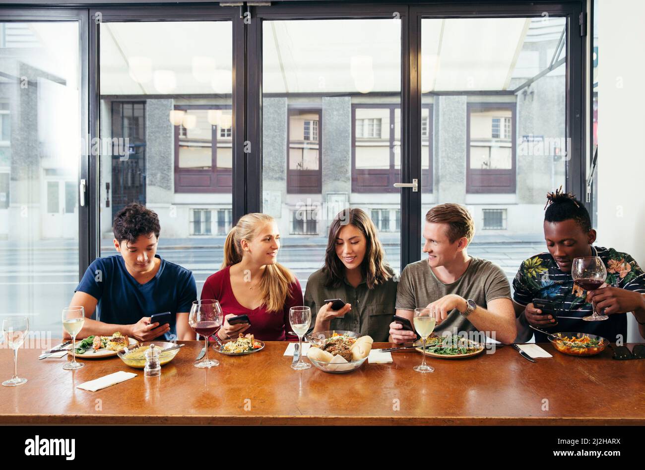 Amis qui prennent leurs repas et regardent les smartphones dans le restaurant Banque D'Images