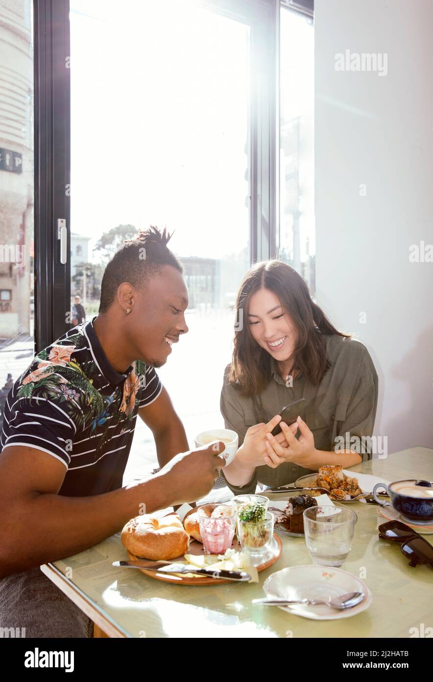 Couple souriant prenant le petit déjeuner et regardant le téléphone intelligent dans le restaurant Banque D'Images