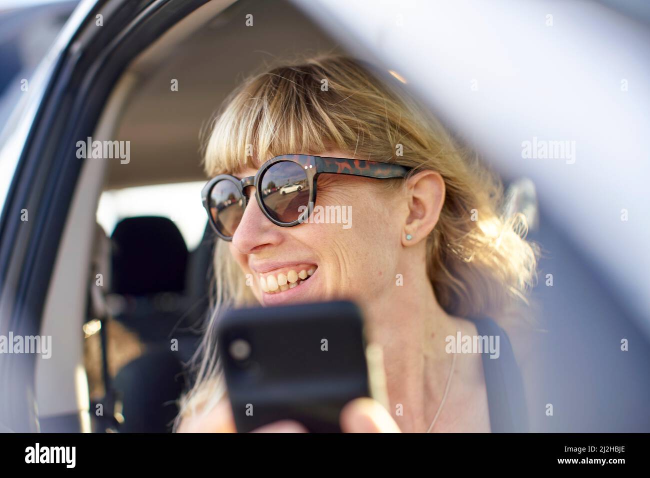Femme mature en lunettes de soleil utilisant un smartphone en voiture Banque D'Images