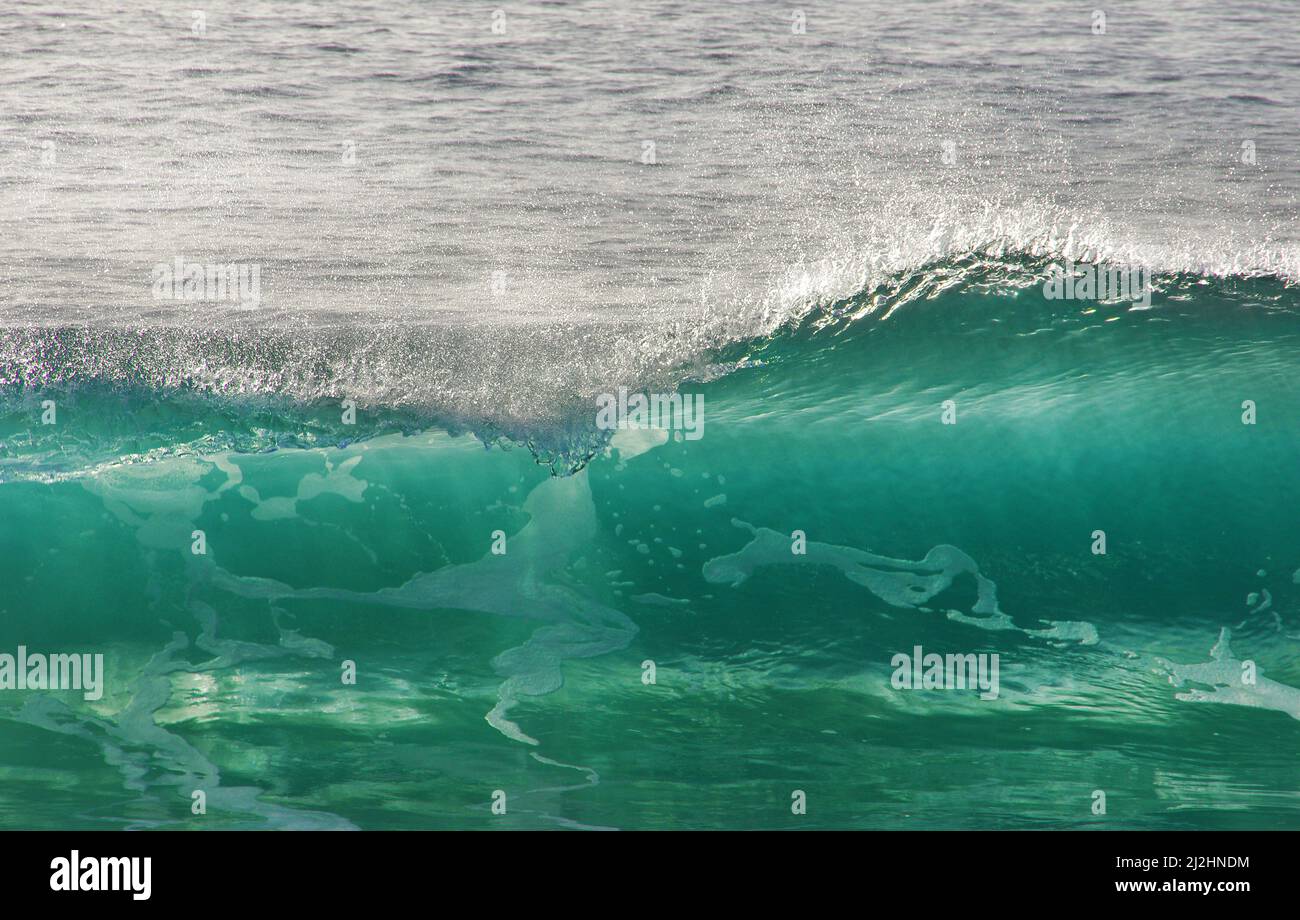 Lumière passant par une onde bleue transparente, avec mise au point sur les gouttes d'eau. Plage de Nazaré, Portugal Banque D'Images