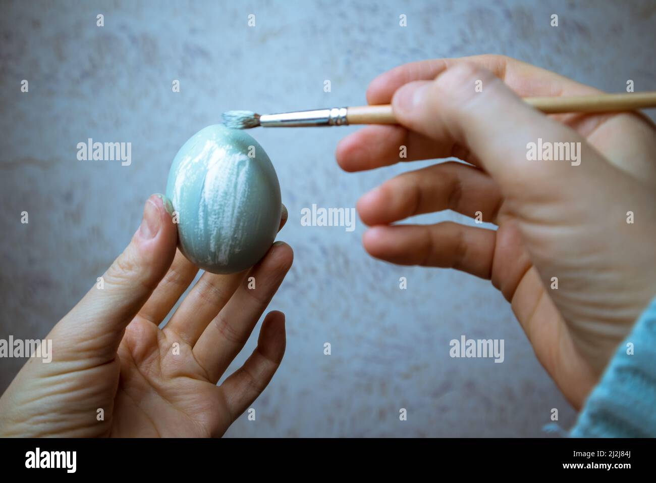 Main tenant un pinceau et peignant un oeuf. Un processus de peinture des oeufs de Pâques avec de la peinture gris-bleu. Pinceau dans la main de femme gros plan. Tradition et Banque D'Images
