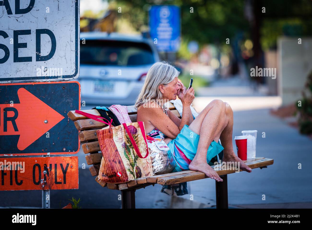 Une vieille femme sans-abri qui pante les sourcils sur un banc du centre-ville de Scottsdale, Arizona, États-Unis. Banque D'Images