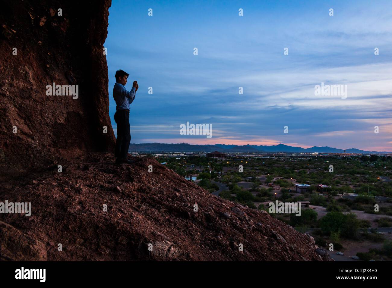 Un jeune homme asiatique capture le ciel du coucher du soleil avec son téléphone du Hole in the Rock à Papago Park, Phoenix, Arizona. Banque D'Images