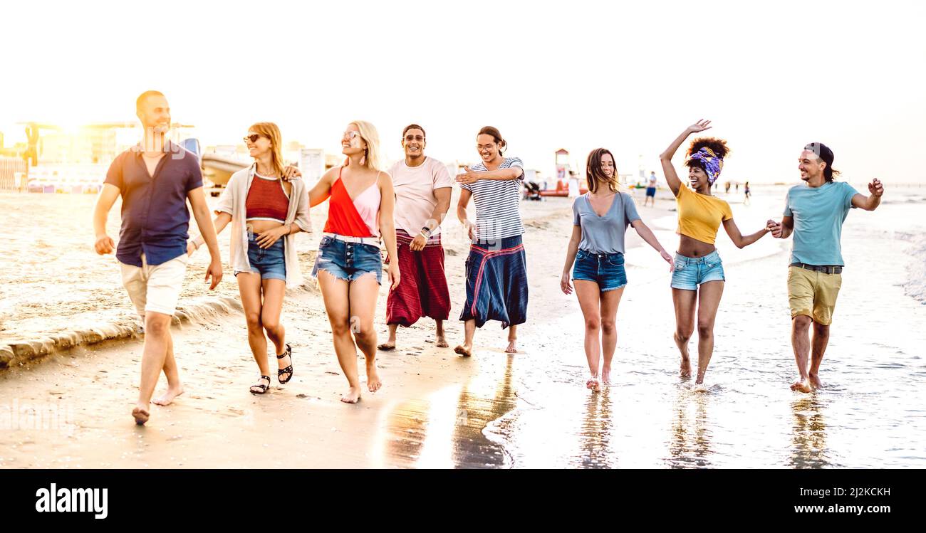 Grand groupe d'amis heureux branchés marchant à la plage à l'heure du coucher du soleil - concept multiracial de style de vie avec les jeunes s'amuser pendant les vacances d'été - Banque D'Images