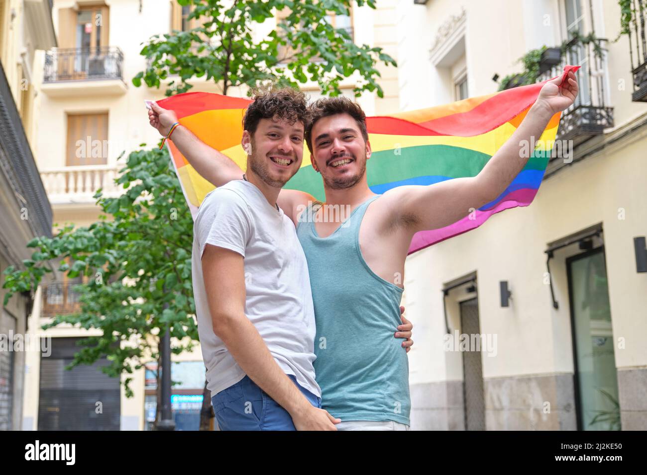 Couple gay souriant et regardant la caméra portant un drapeau LGBT. Banque D'Images