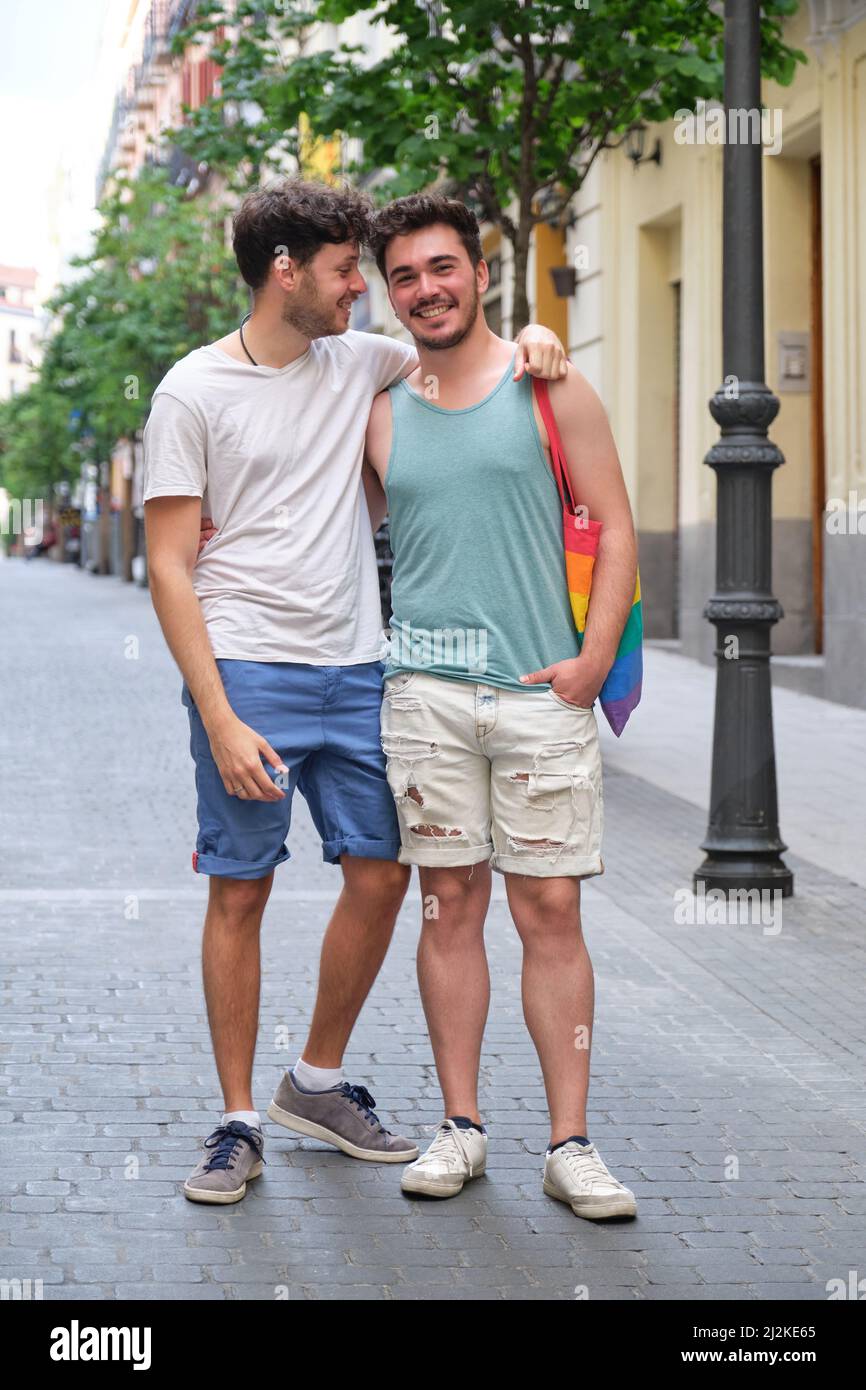 Un couple gay riant en train de se serrer et de regarder un appareil photo dans la rue. Banque D'Images