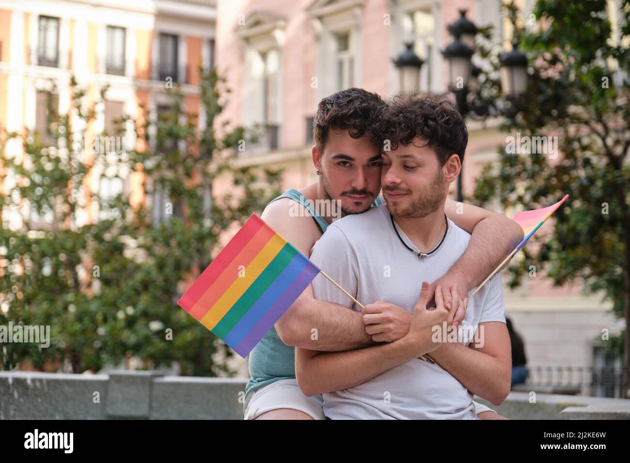 Couple gay embrassant et souriant tenant des drapeaux LGBT assis près d'une police. Banque D'Images