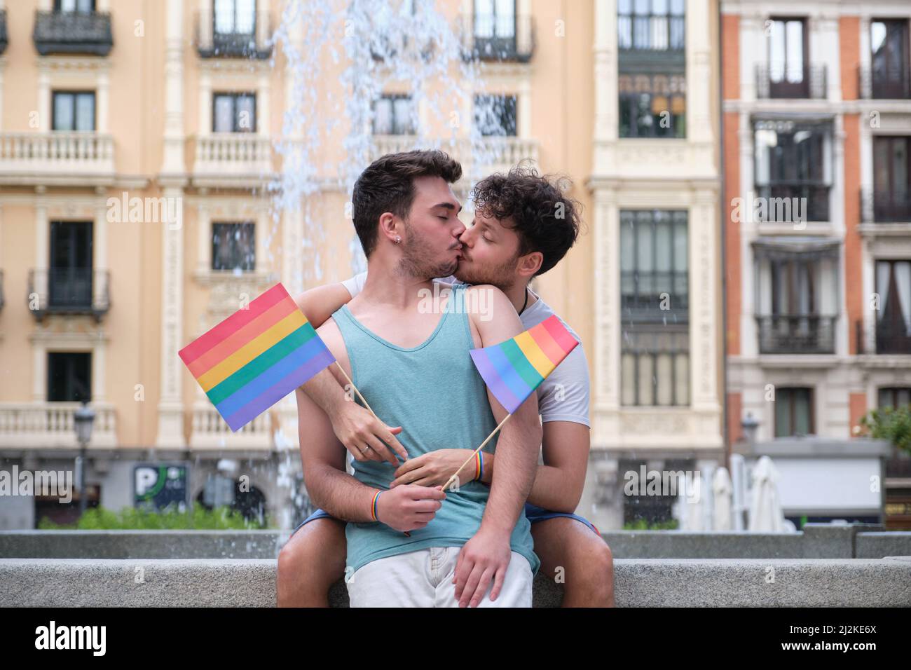 Un couple gay riant et embrassant assis sur un banc tenant des drapeaux LGBT. Banque D'Images