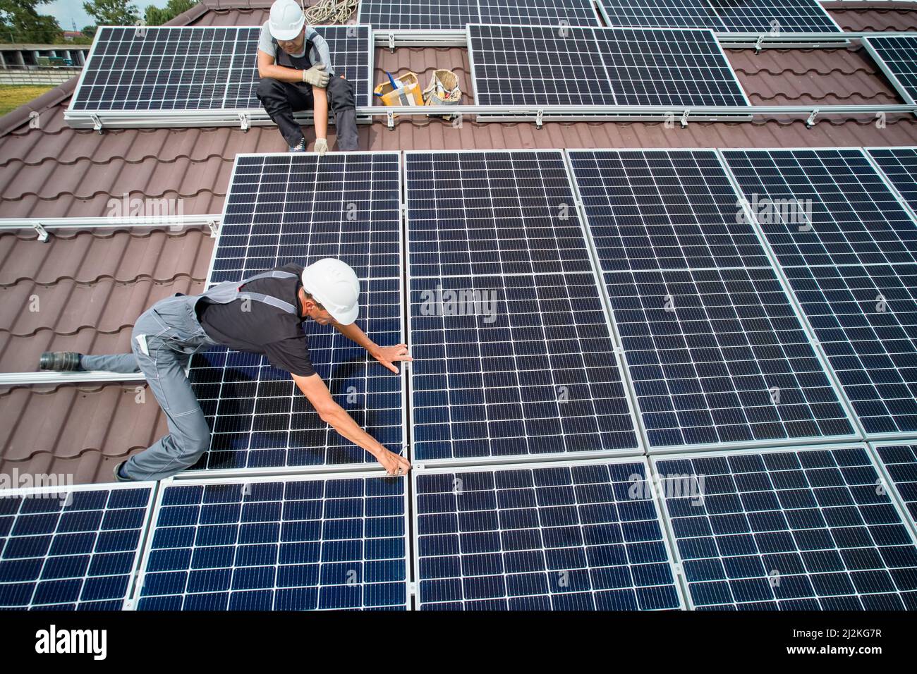 Hommes installateurs installation de modules solaires photovoltaïques sur le toit de la maison. Ingénieurs en casques de construction de panneaux solaires à l'extérieur. Concept d'énergie alternative et renouvelable. Vue aérienne. Banque D'Images