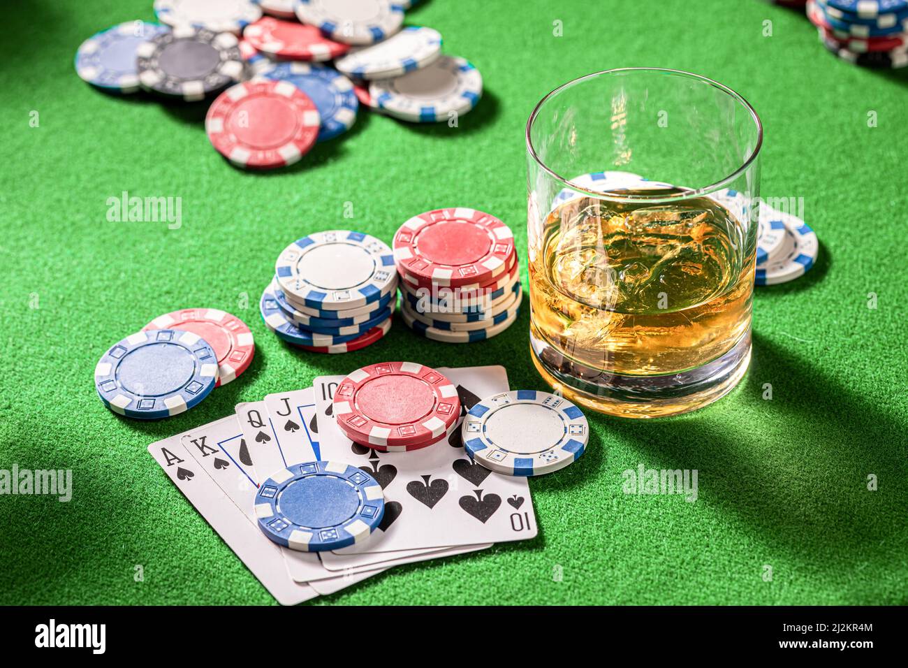 Table de jeu verte avec whisky, cartes et jetons. Verre de bourbon avec glace sur table de jeu avec cartes et jetons. Banque D'Images