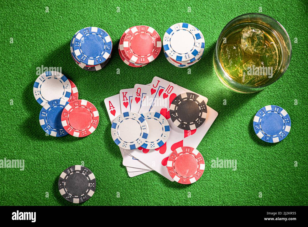 Table verte pour le poker avec whisky, cartes et jetons. Verre de bourbon avec glace sur table de jeu avec cartes et jetons. Banque D'Images