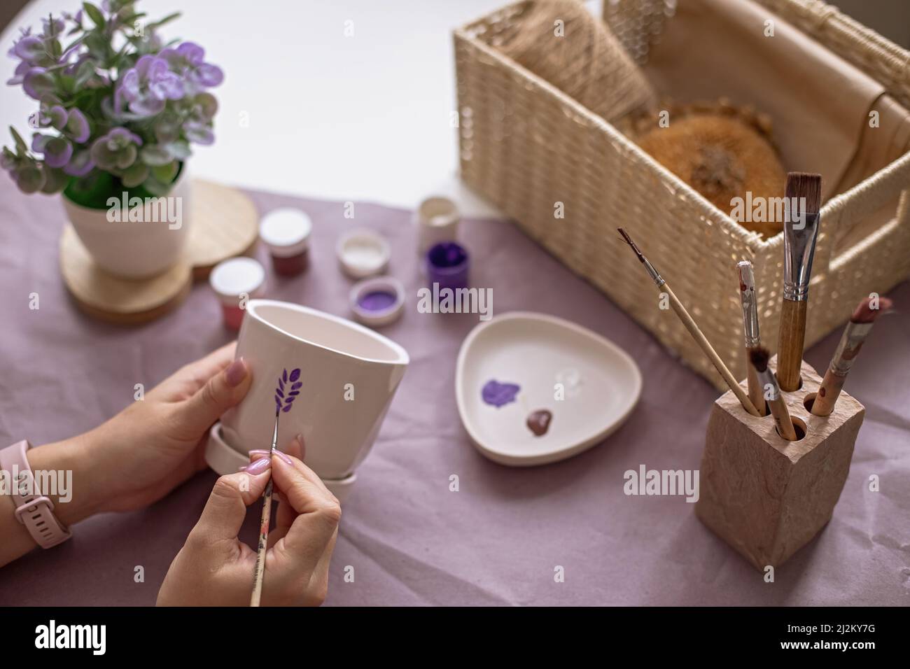 Les mains des femmes peignent un pot en céramique blanc de fleur sur la table Banque D'Images