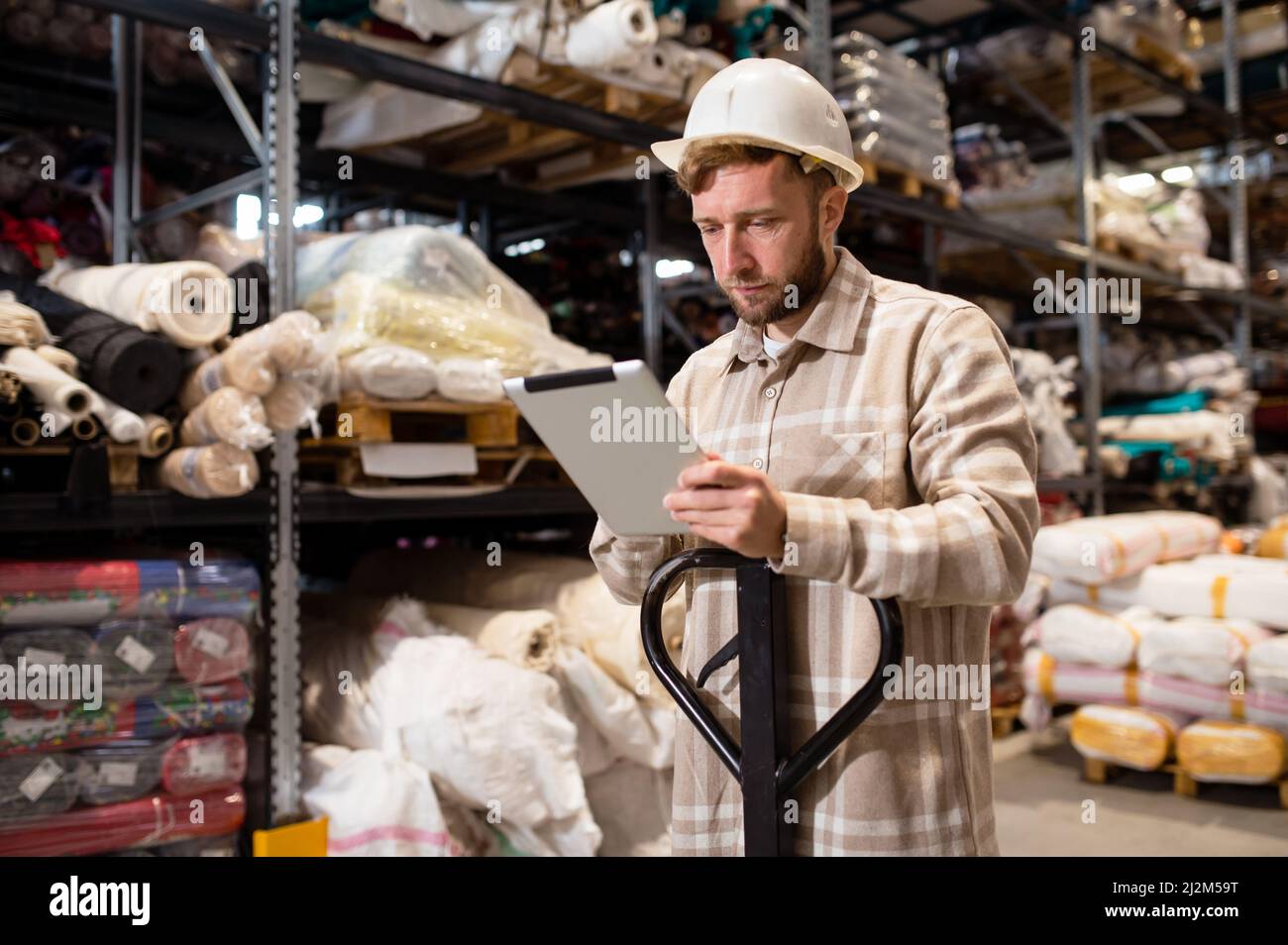Un homme heureux travaillant en usine avec une tablette numérique à proximité des rouleaux de matériaux empilés Banque D'Images