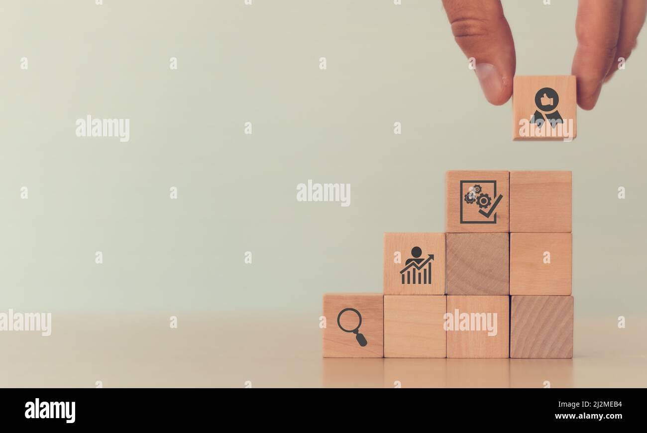 Concept de contrôle de la qualité dans l'industrie. La main de l'homme met les cubes en bois empilés dans les escaliers avec l'icône de processus de contrôle de qualité; trouver, évaluation, impro Banque D'Images