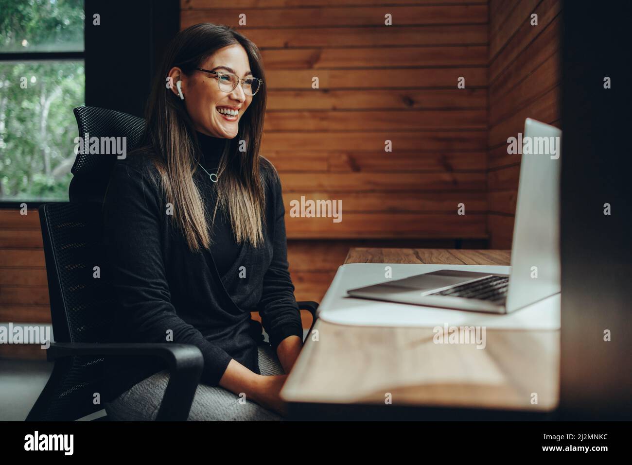 Femme entrepreneur ayant une réunion en ligne dans un espace de travail commun moderne. Une jeune femme d'affaires heureuse qui communique avec ses associés d'affaires pendant Banque D'Images