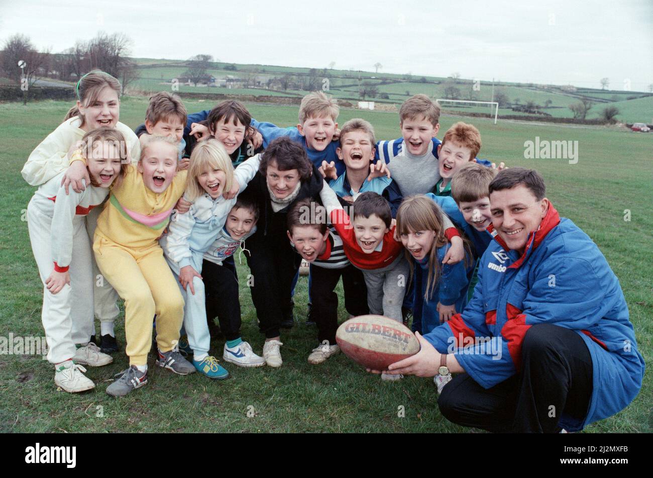 Quand Stephen Deakin, responsable du développement de la ligue de rugby de Kirklees, est arrivé à la Thurstonland Junior School pour enseigner aux élèves les bases de la ligue de rugby, tout le monde a rejoint... y compris le professeur Kay Martin, photographié au milieu de la mêlée. Et, à en juger par les expressions, les filles l'aimaient autant que les garçons. Deakin (à droite) fait une tournée des écoles juniors dans la région dans une tentative de diffuser le jeu. 16th mars 1990. Banque D'Images