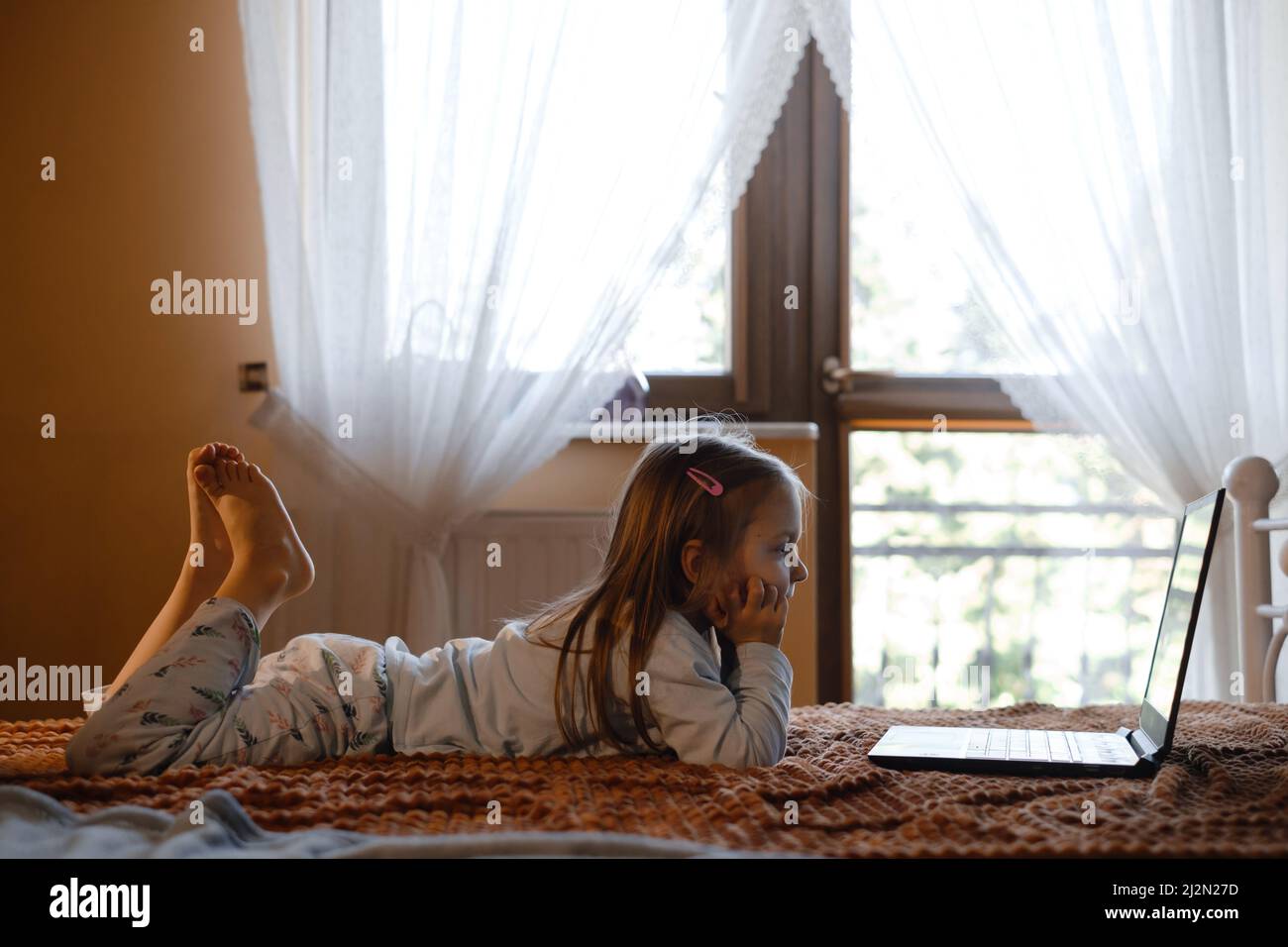 Enfants regardant des dessins animés sur un ordinateur portable. Enfant sérieux avec la technologie à la maison sur le lit passer du temps en ligne. Éducation et divertissement pour les tout-petits. Une fille Banque D'Images