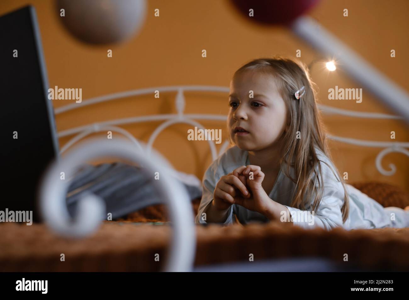 Enfants regardant des dessins animés sur un ordinateur portable. Enfant sérieux avec la technologie à la maison sur le lit passer du temps en ligne. Éducation et divertissement pour les tout-petits. Une fille Banque D'Images