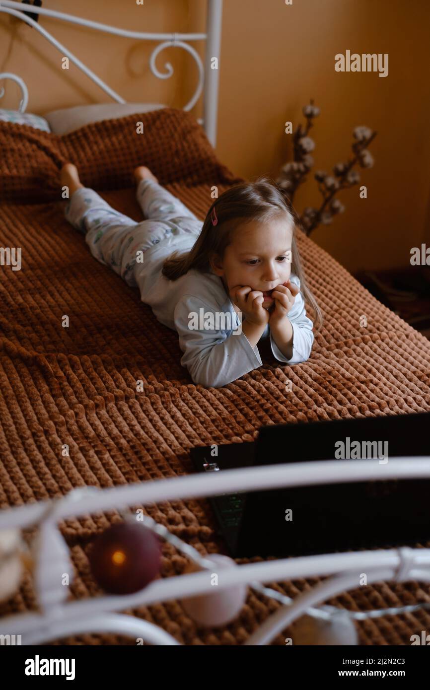 Enfants regardant des dessins animés sur un ordinateur portable. Enfant sérieux avec la technologie à la maison sur le lit passer du temps en ligne. Éducation et divertissement pour les tout-petits. Une fille Banque D'Images