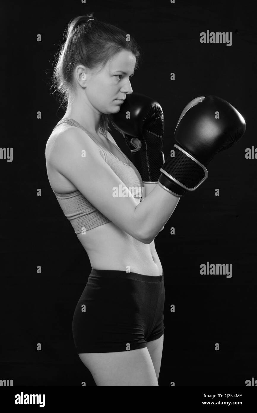 Joli boxeur thaïlandais Muay en posture d'attaque. Fitness jeune femme entraînement de boxe sur fond noir, gros plan monochrome Banque D'Images