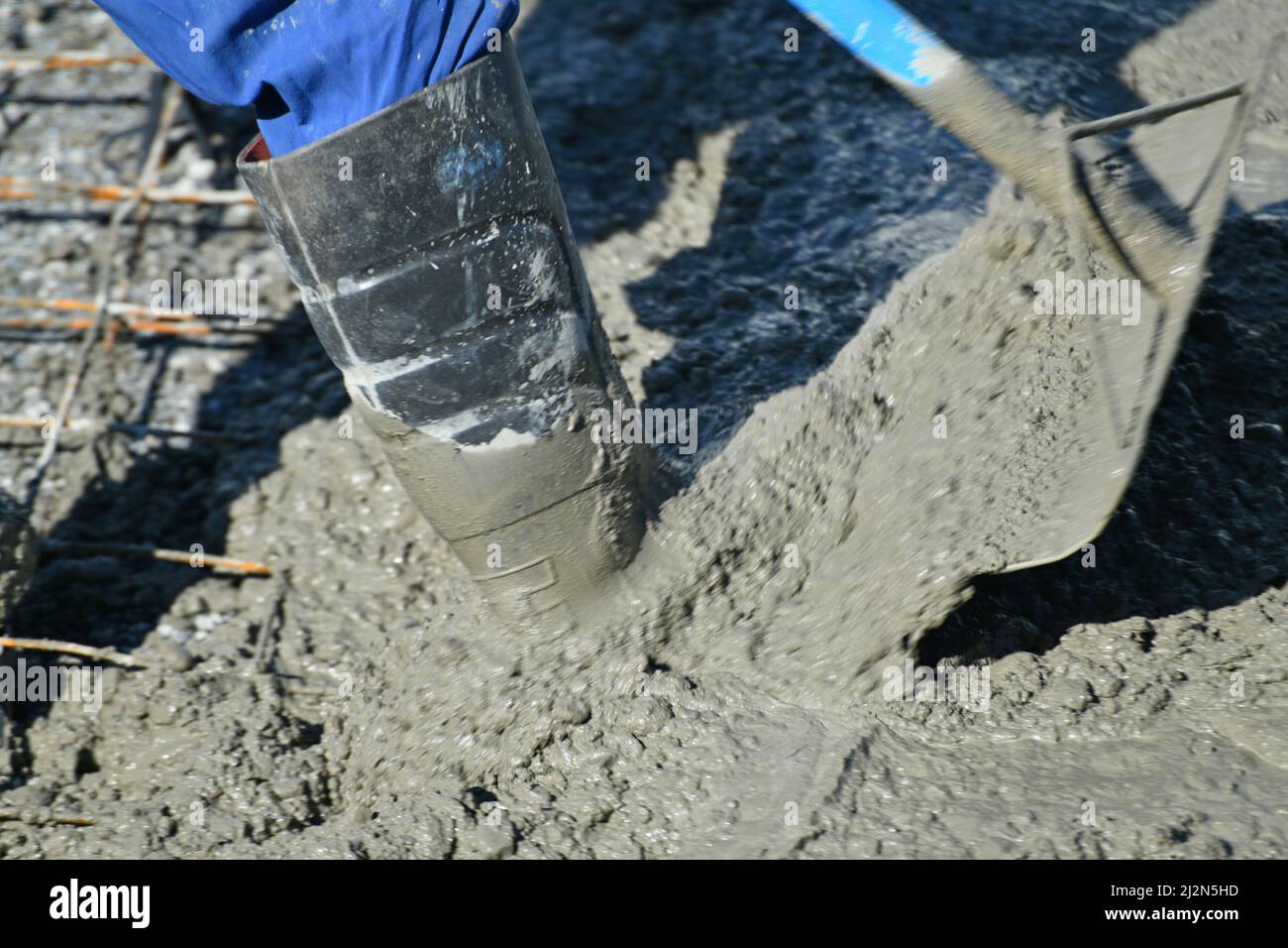 Un constructeur tient la cheville profondément dans le ciment humide tout en déplaçant le ciment pendant un versement de béton Banque D'Images