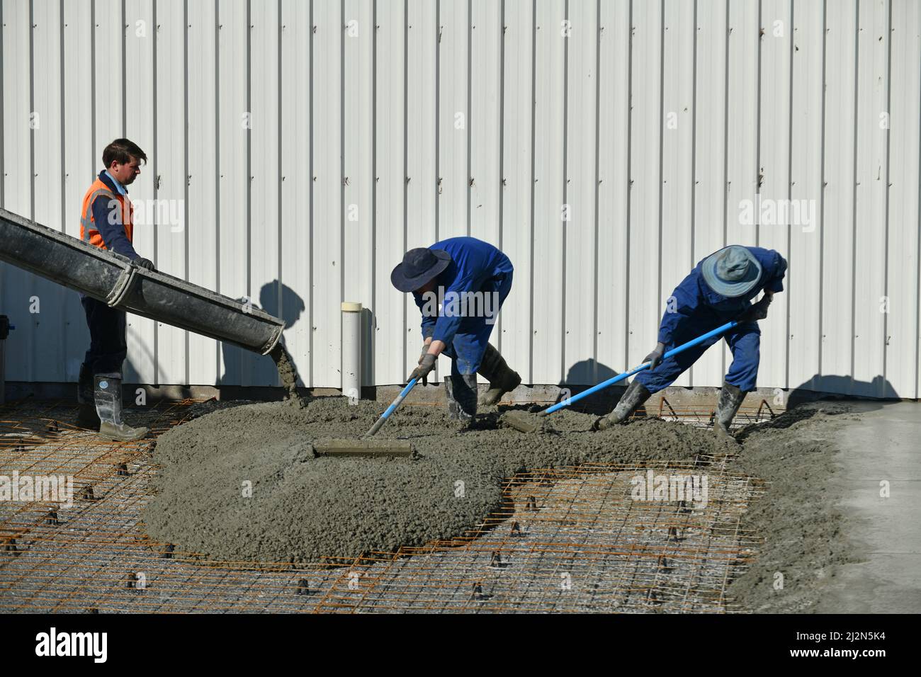 les constructeurs répandent le ciment nouvellement versé pour une dalle de béton Banque D'Images