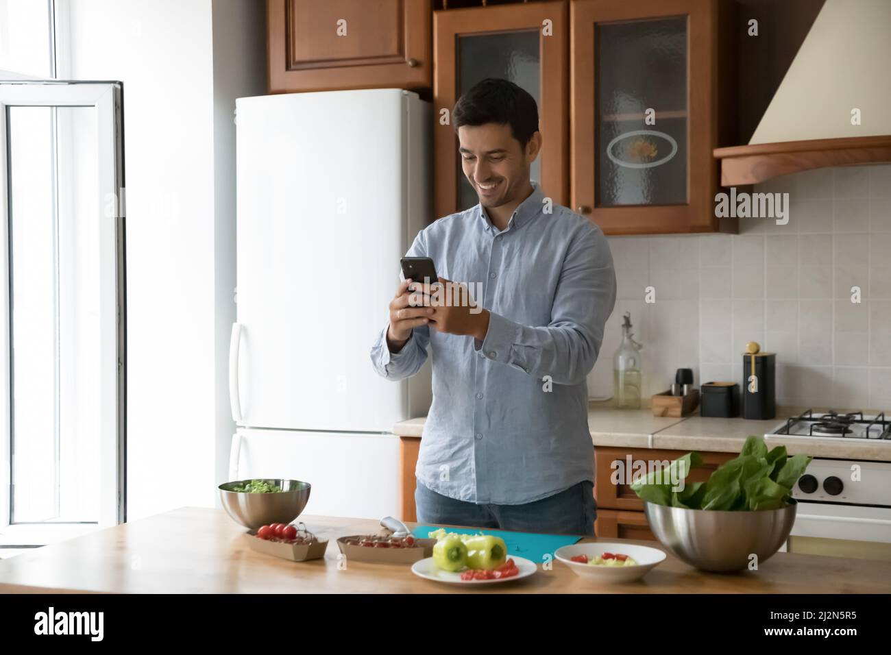 Joyeux jeune homme de chef cuisinier lisant la recette sur smartphone Banque D'Images