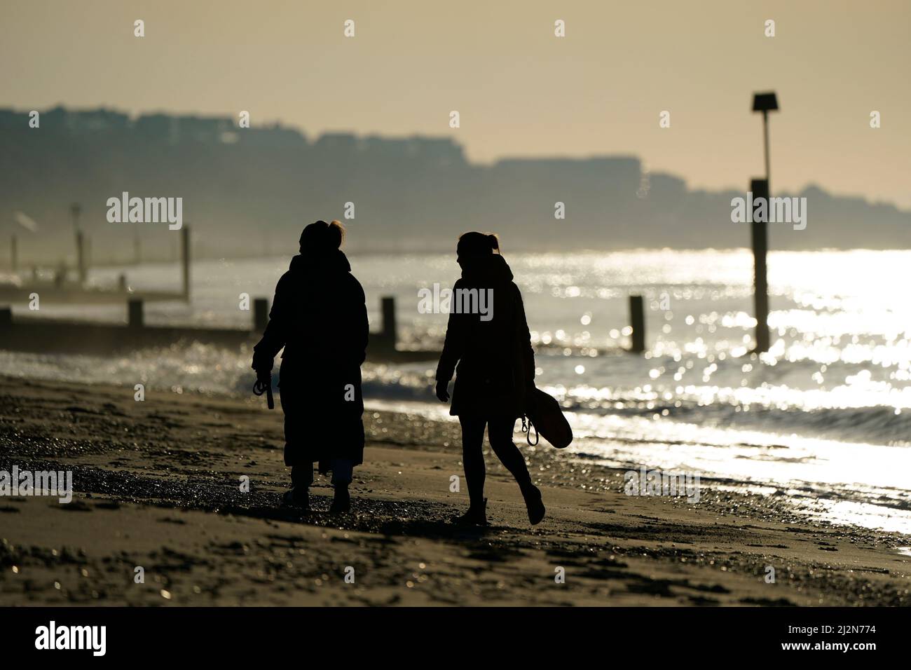 Les gens marchent le long de la plage tandis que le soleil se lève sur la plage de Boscombe à Dorset. Date de la photo: Dimanche 3 avril 2022. Banque D'Images