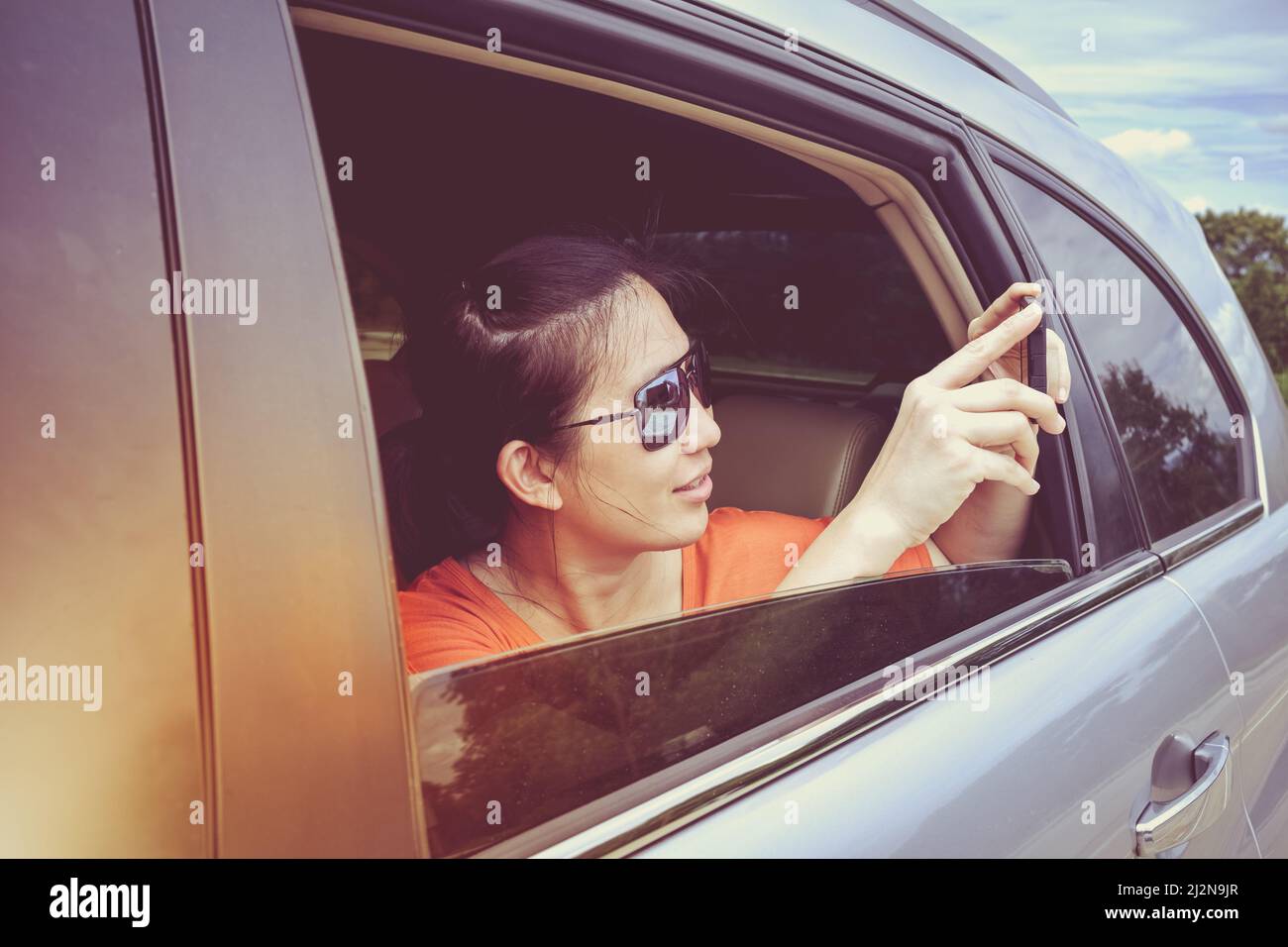 Bonne femme asiatique tenant un téléphone portable et prenant des photos tout en étant assise dans la voiture. Le voyageur saisit un moment de voyage idéal en vacances. Banque D'Images