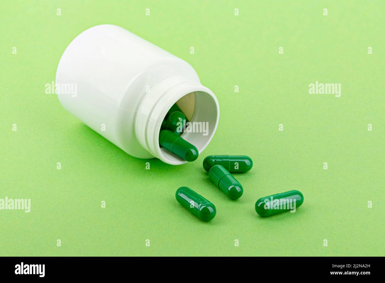 Capsules de médicaments versant d'une bouteille de pilule, fond vert. Banque D'Images