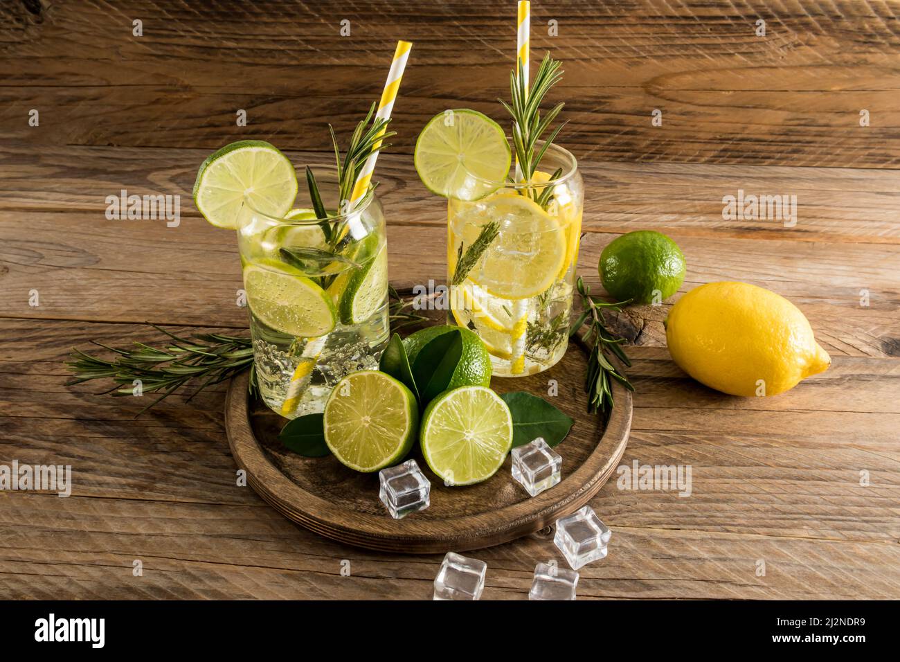deux verres d'eau vitaminée au citron et à la chaux, des brins de romarin sur un plateau rond en bois et une table de village. glaçons pour refroidir Banque D'Images