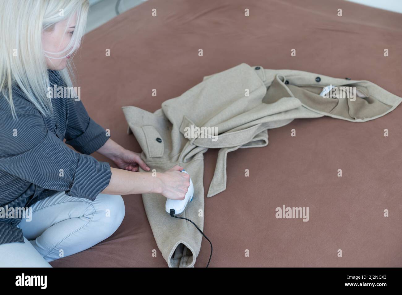 Dispositif sans fil pour le nettoyage des tissus tricotés contre les peluches. La femme retire les peluches du pull. Banque D'Images
