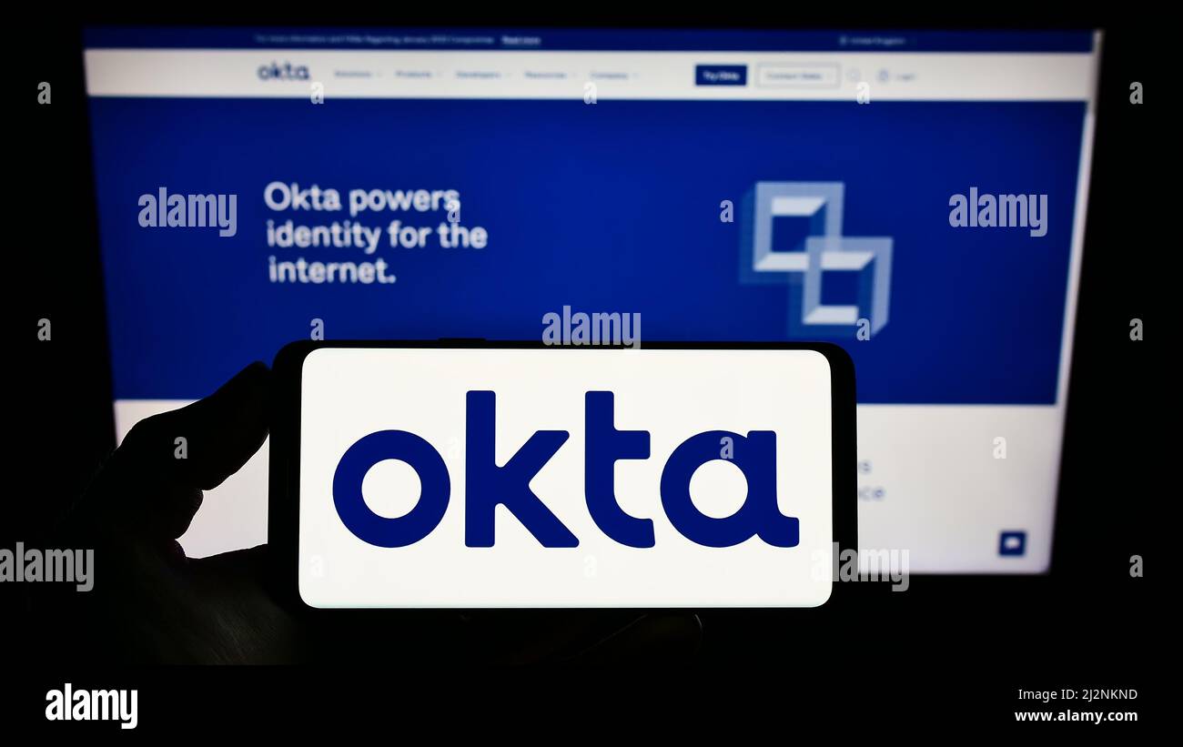 Personne détenant un smartphone avec le logo de la société américaine de gestion de l'identité Okta Inc. À l'écran devant le site Web. Mise au point sur l'affichage du téléphone. Banque D'Images