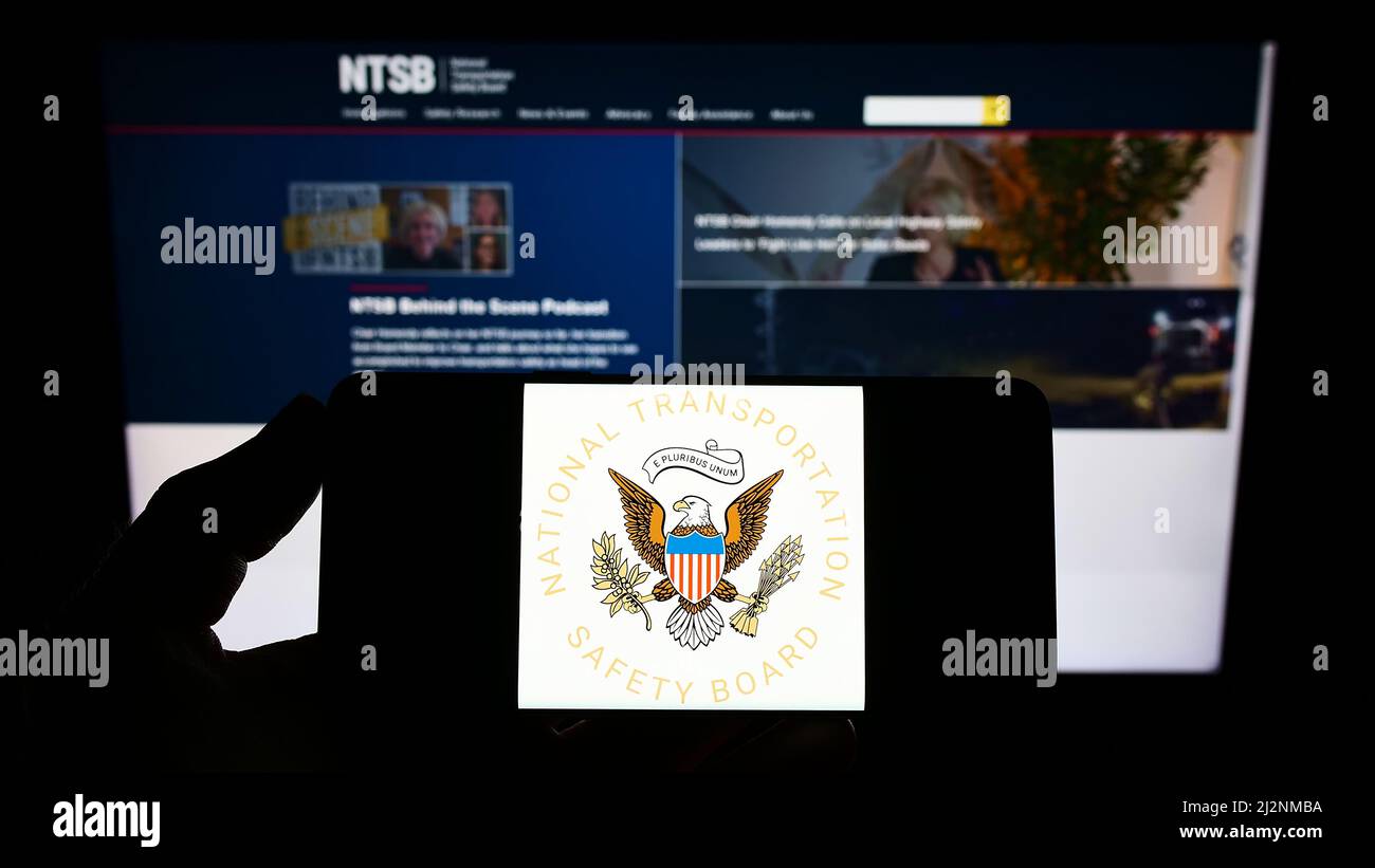 Personne tenant un smartphone avec le sceau du National Transportation Safety Board (NTSB) des États-Unis sur l'écran devant le site Web. Mise au point sur l'affichage du téléphone. Banque D'Images Personne tenant un smartphone avec le sceau du National Transportation Safety Board (NTSB) des États-Unis sur l'écran devant le site Web. Mise au point sur l'affichage du téléphone. Banque D'Images