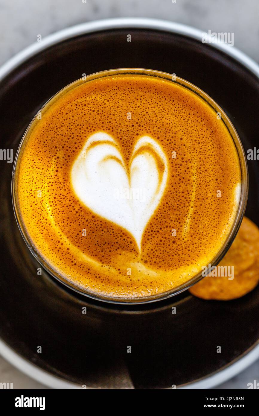 Tasse de café latte dans un verre, avec l'amour coeur latte art et un cookie sur le côté. Image verticale. Banque D'Images