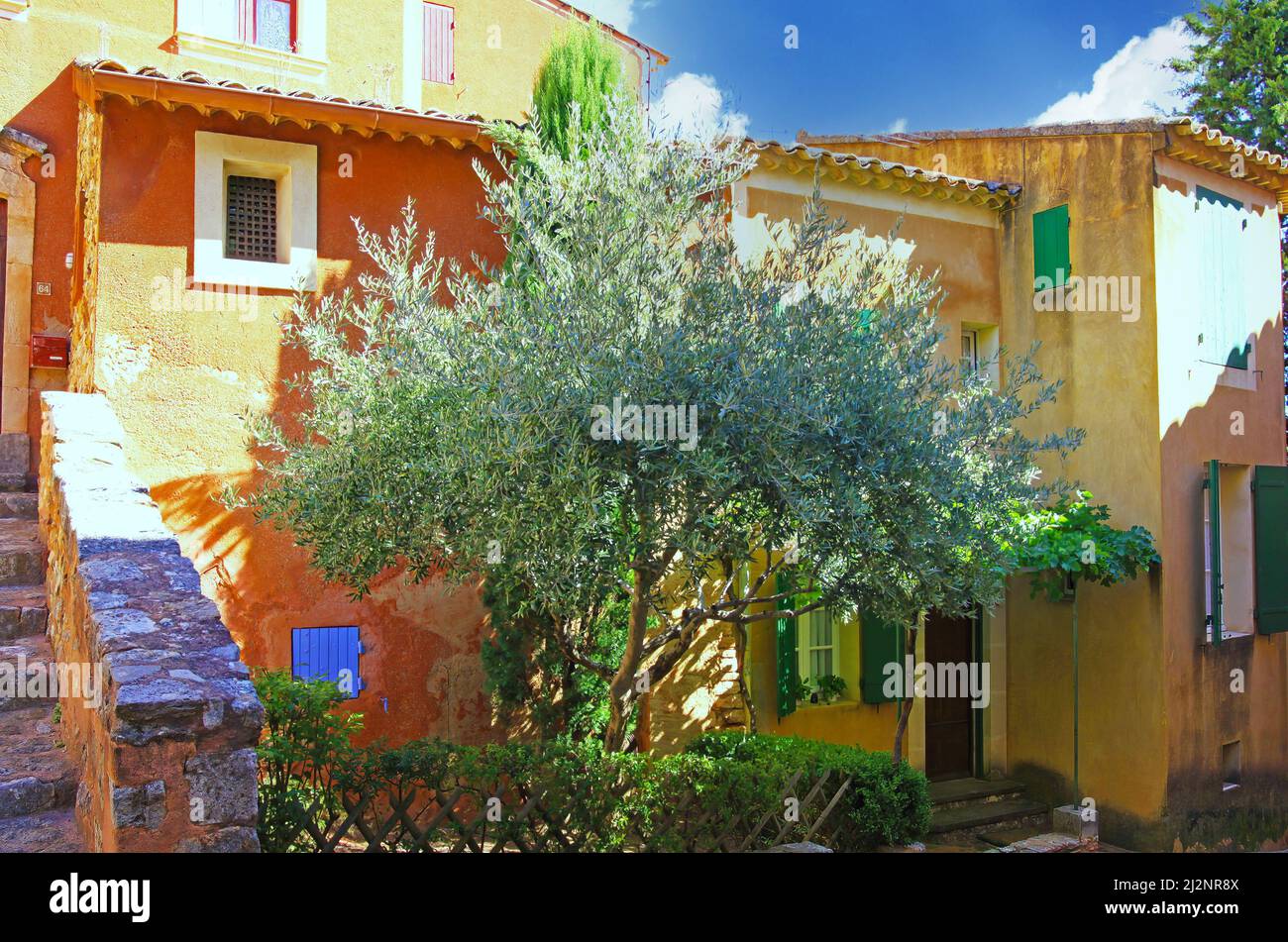 Roussillon, France - octobre 9. 2019: Vue sur la maison traditionnelle en pierre naturelle ocre avec grand olivier vert dans cour avant colorée Banque D'Images