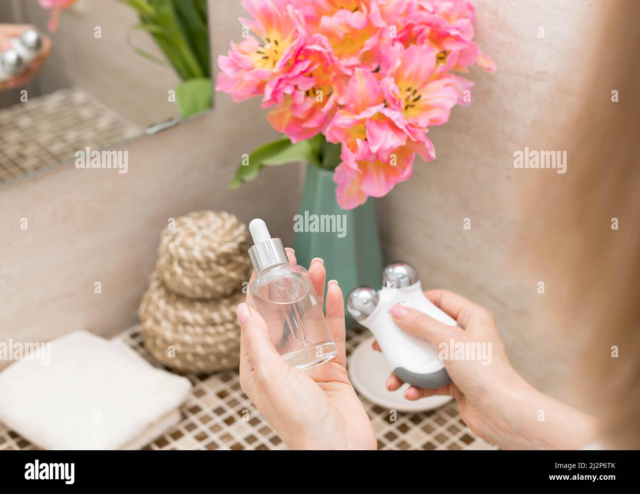Mains de femmes portant du sérum de beauté et un appareil de tonification du visage à micro-courant Banque D'Images