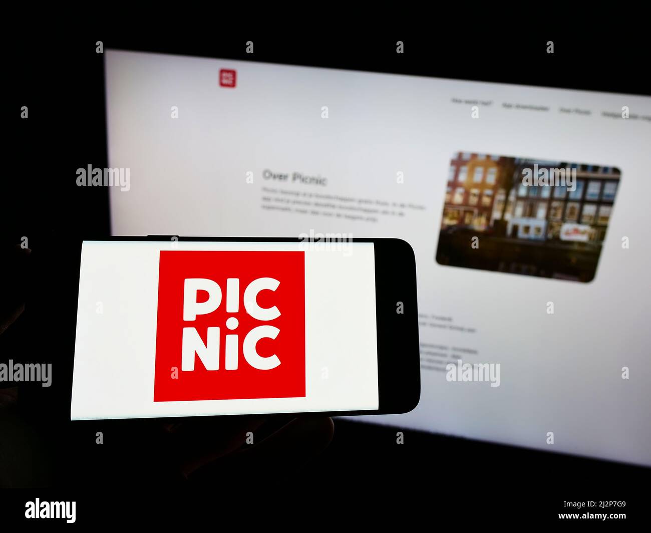 Personne tenant un téléphone portable avec le logo de la société néerlandaise de supermarché en ligne Picnic B.V. à l'écran en face de la page Web. Mise au point sur l'affichage du téléphone. Banque D'Images
