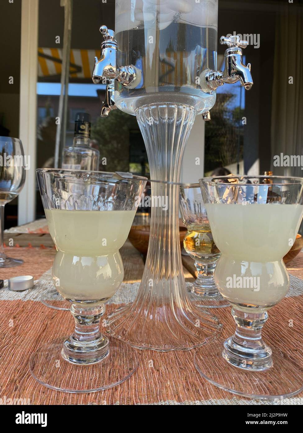 Fontaine à l'absinthe avec eau et cube de glace, quatre verres et une cuillère. Célébration en plein air sous le soleil. Banque D'Images