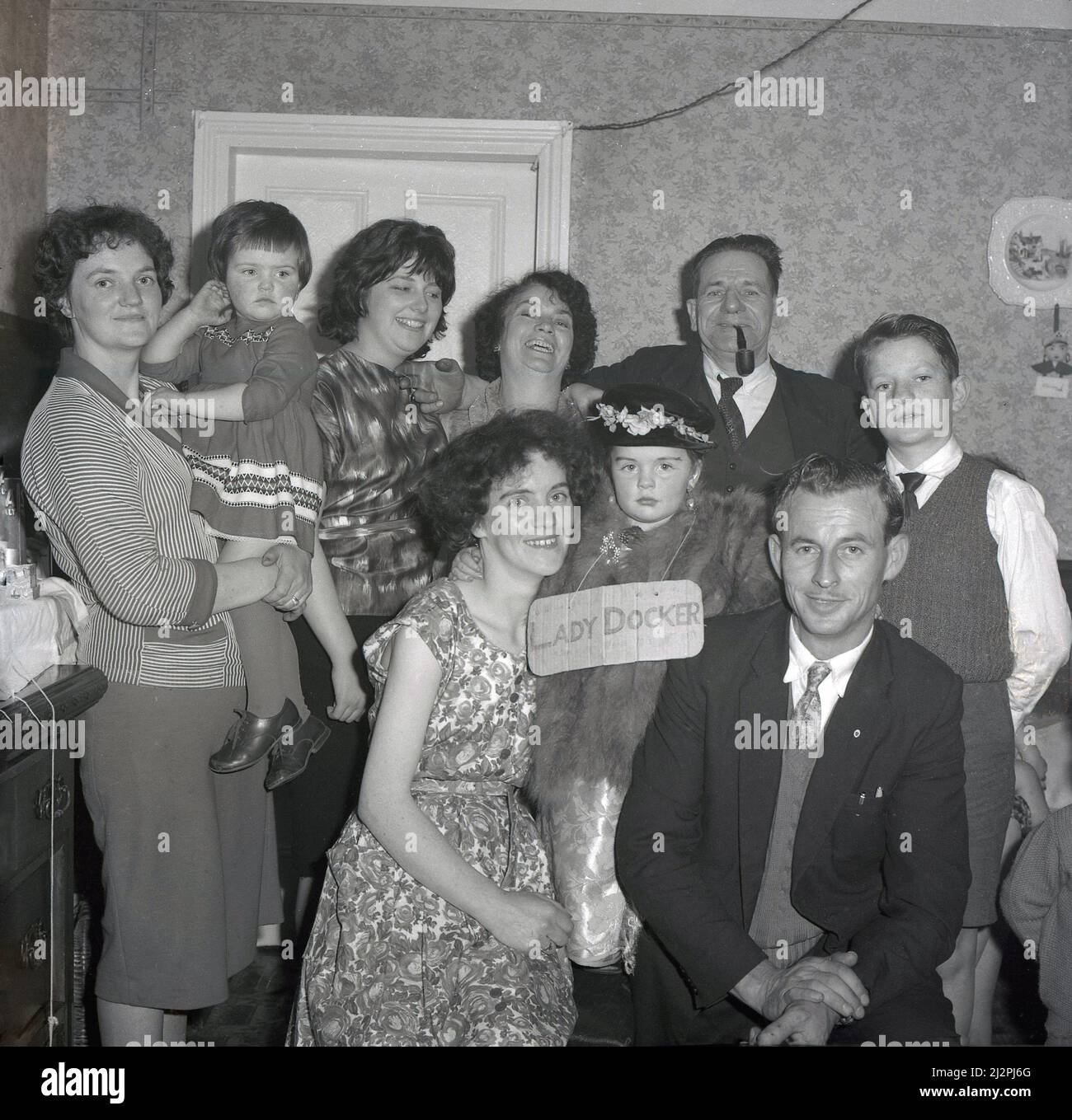 1961, historique, avec sa mère, son père et d'autres membres de la famille célébrant son anniversaire, une jeune fille s'habille, comme le signe de carton sur elle dit, comme «Lady Docker», Stockport, Manchester, Angleterre, ROYAUME-UNI. En Grande-Bretagne d'après-guerre, Lady Docker, née Norah Royce Turner dans un appartement au-dessus d'une boucherie à Derby, était une « personnalité » des médias, une socialite. Par le mariage, en particulier son troisième mariage avec Sir Bernard Docker, président de la compagnie automobile Daimler et directeur de la banque Midland, elle a mené une vie colouable et extravagante pour l'époque, mais elle n'a jamais oublié ses humbles racines de classe ouvrière. Banque D'Images